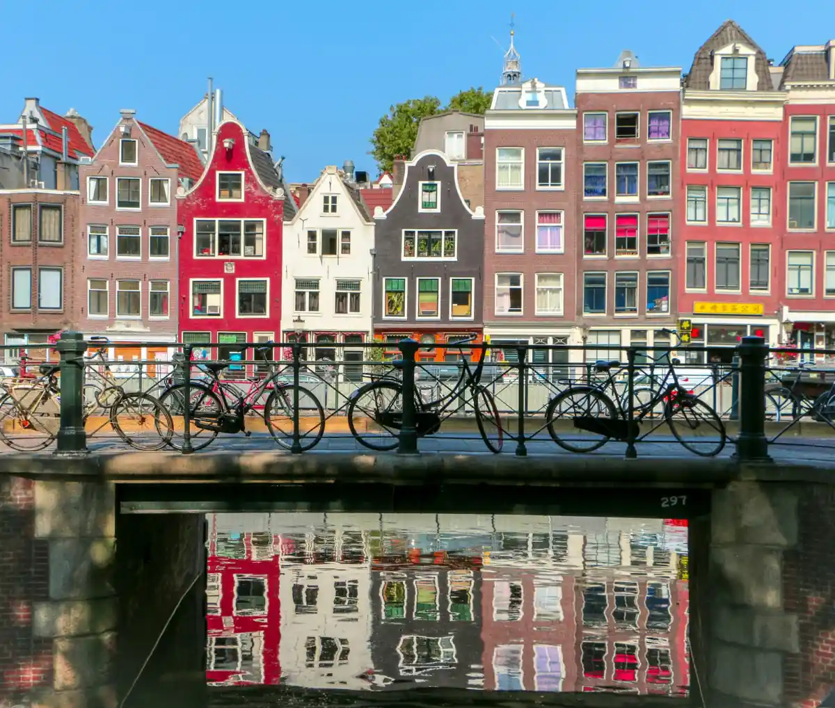 Bicycles parked on a canal bridge in Amsterdam in front of tall, narrow canal houses.