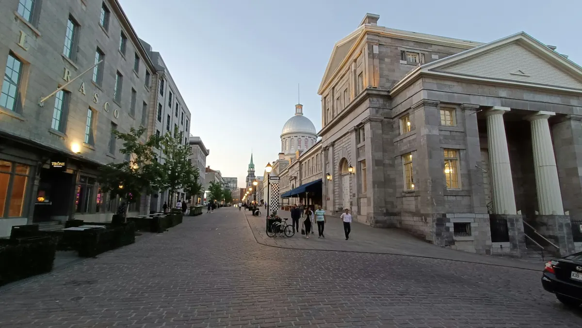 A cobblestone street in Old Montreal lined with stone buildings and a domed market hall.