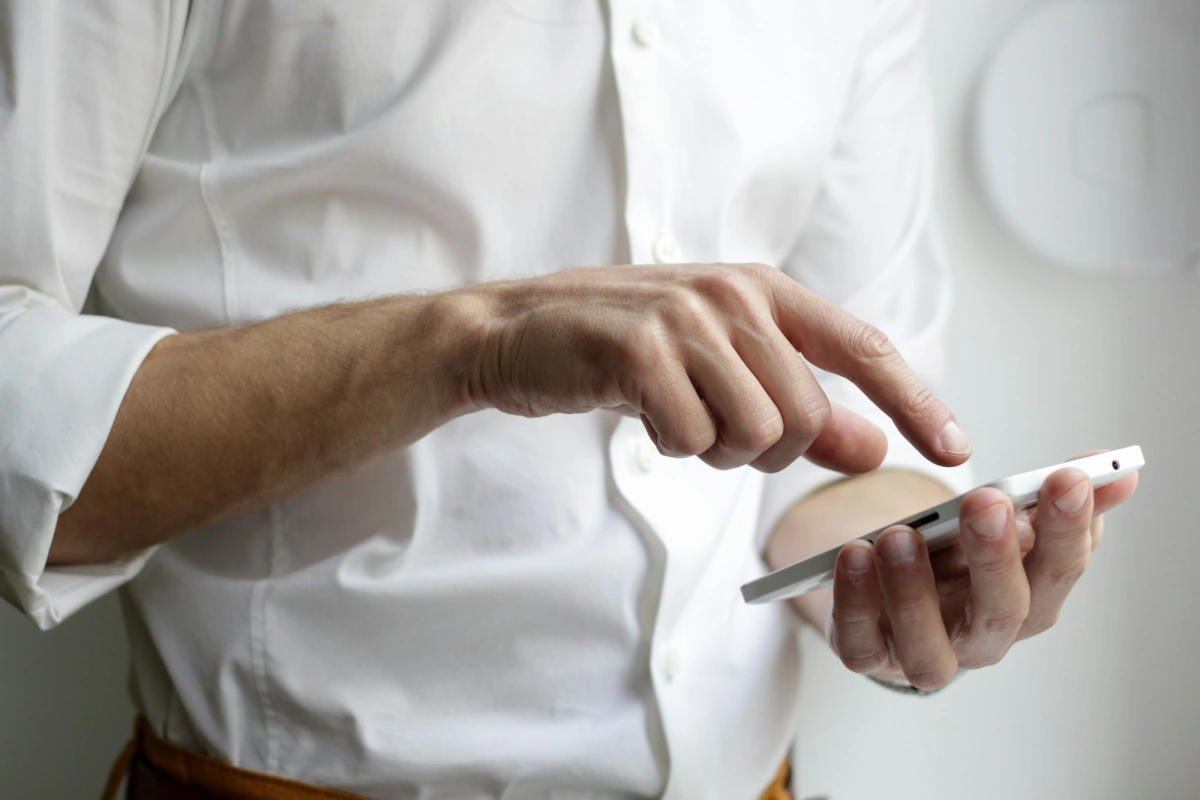 A man in a white shirt tapping on a smartphone held in one hand.
