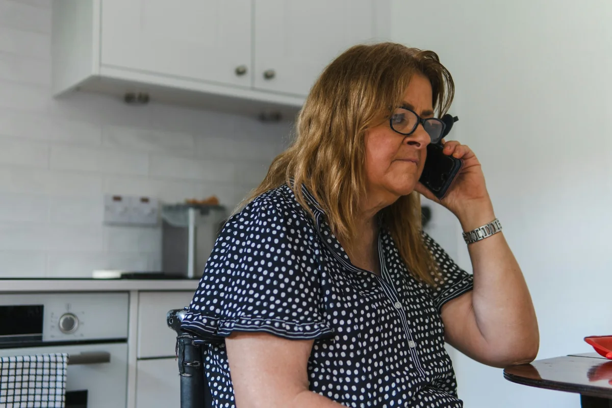 A woman in glasses talking on her mobile phone at a kitchen table.